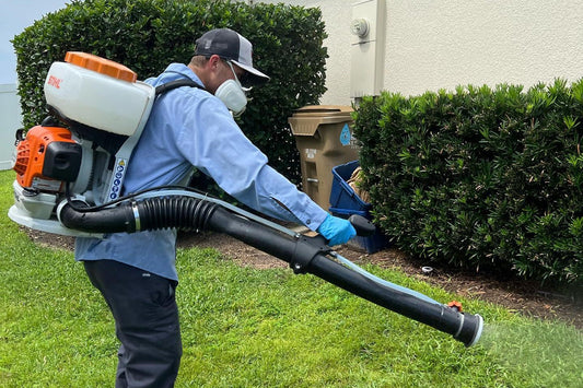 Webenex technician in a respirator misting landscaping with a backpack mist blower
