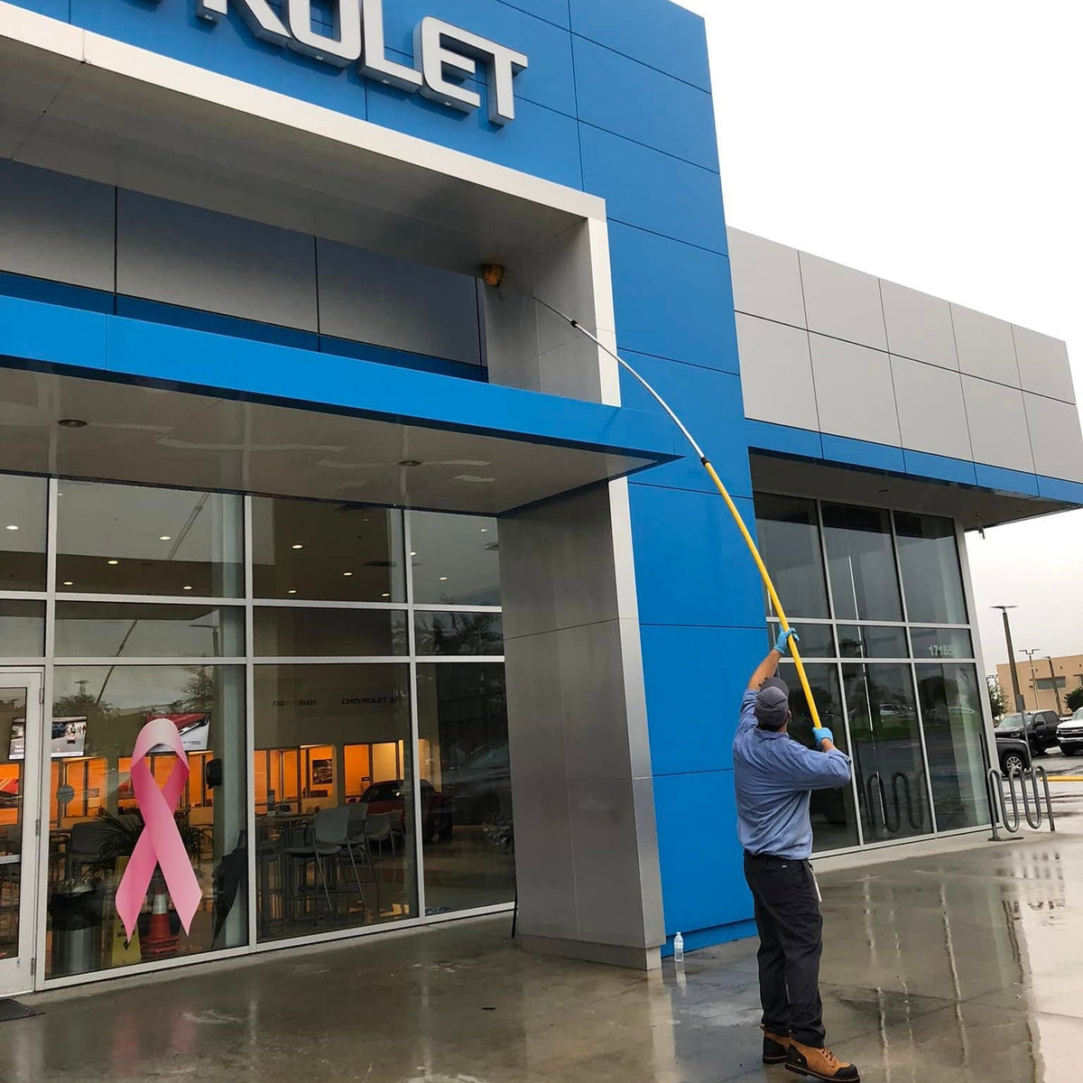 A Webenex technician de-webbing a car dealership storefront with an extension pole