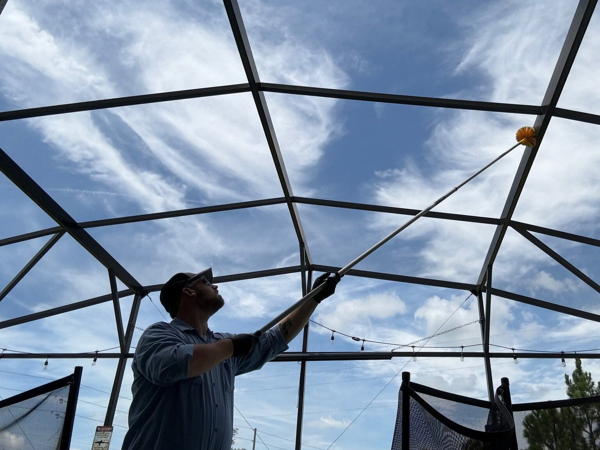 A Webenex technician de-webbing a pool cage with a long pole brush