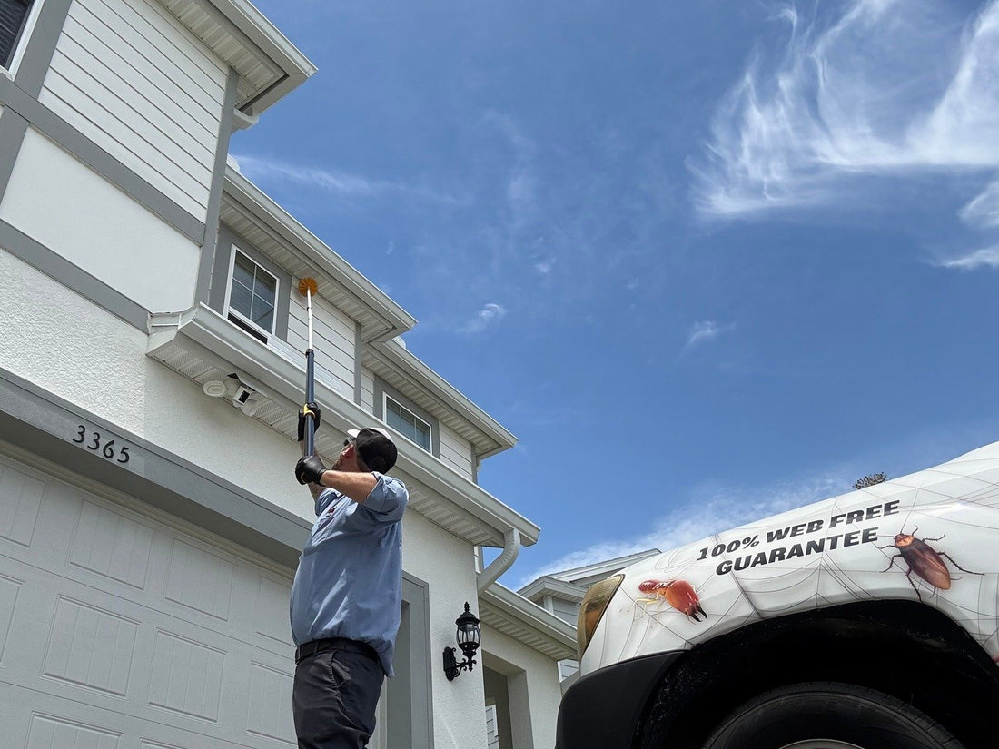 A Webenex technician treating a second-story eave with the Webenex truck in the driveway